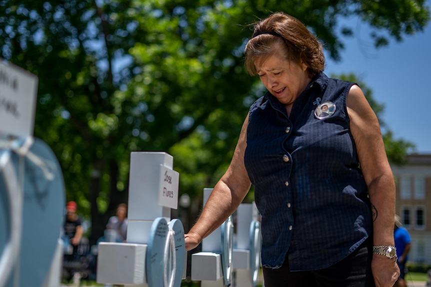 An older woman cries as she touches a hand to a white cross with a heart shape strapped to the front