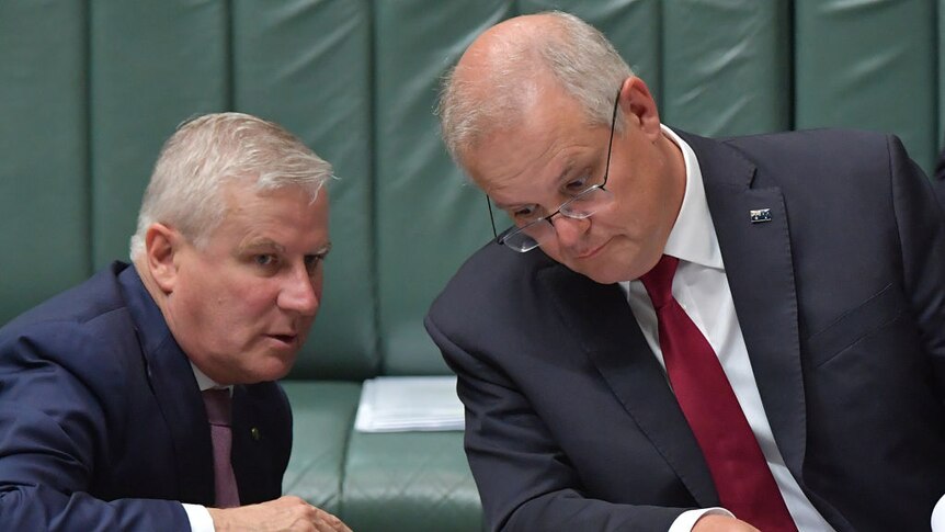 Scott Morrison leans towards Michael McCormack in Parliament listening intently to what he is saying