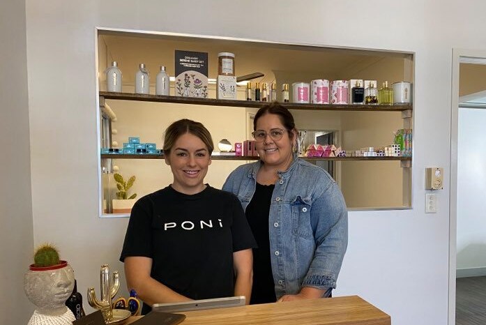 Two women stand behind a counter in shop and smile at the camera