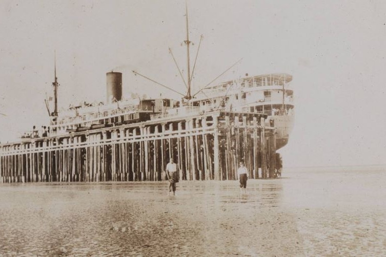 A sepia photo of a ship docked at low tide.