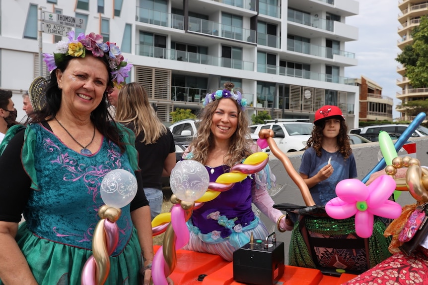 Two women dressed like fairies, in colourful clothing, holding balloons.