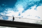 A person walks over a highway using a footbridge on a blue sky day.