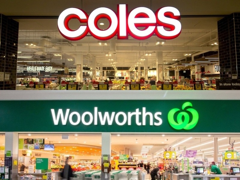 Illuminated logos of Coles and Woolworths outside of each supermarket in a shopping centre.