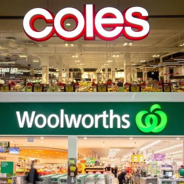 Illuminated logos of Coles and Woolworths outside of each supermarket in a shopping centre.