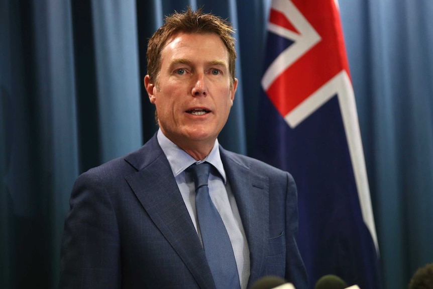 A mid shot of Attorney-General Christian Porter at a media conference with an Australian flag over his left shoulder.