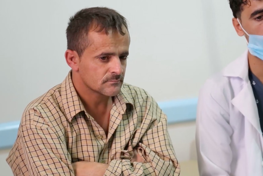 Abro Ibrahim speaks to doctors in the hospital where his son is being treated, he is wearing a white button-up shirt