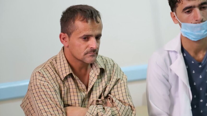 Abro Ibrahim speaks to doctors in the hospital where his son is being treated, he is wearing a white button-up shirt