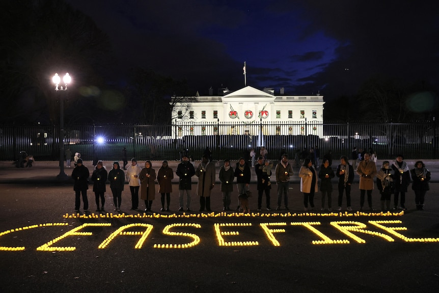 A group of people is pictured standing in front of the White House in the dark, in front of them candles that spell 'ceasefire'