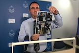 An NT police officer shows images of a man police wish to speak with in relation to a fatal hit-and-run on New Year's Eve.