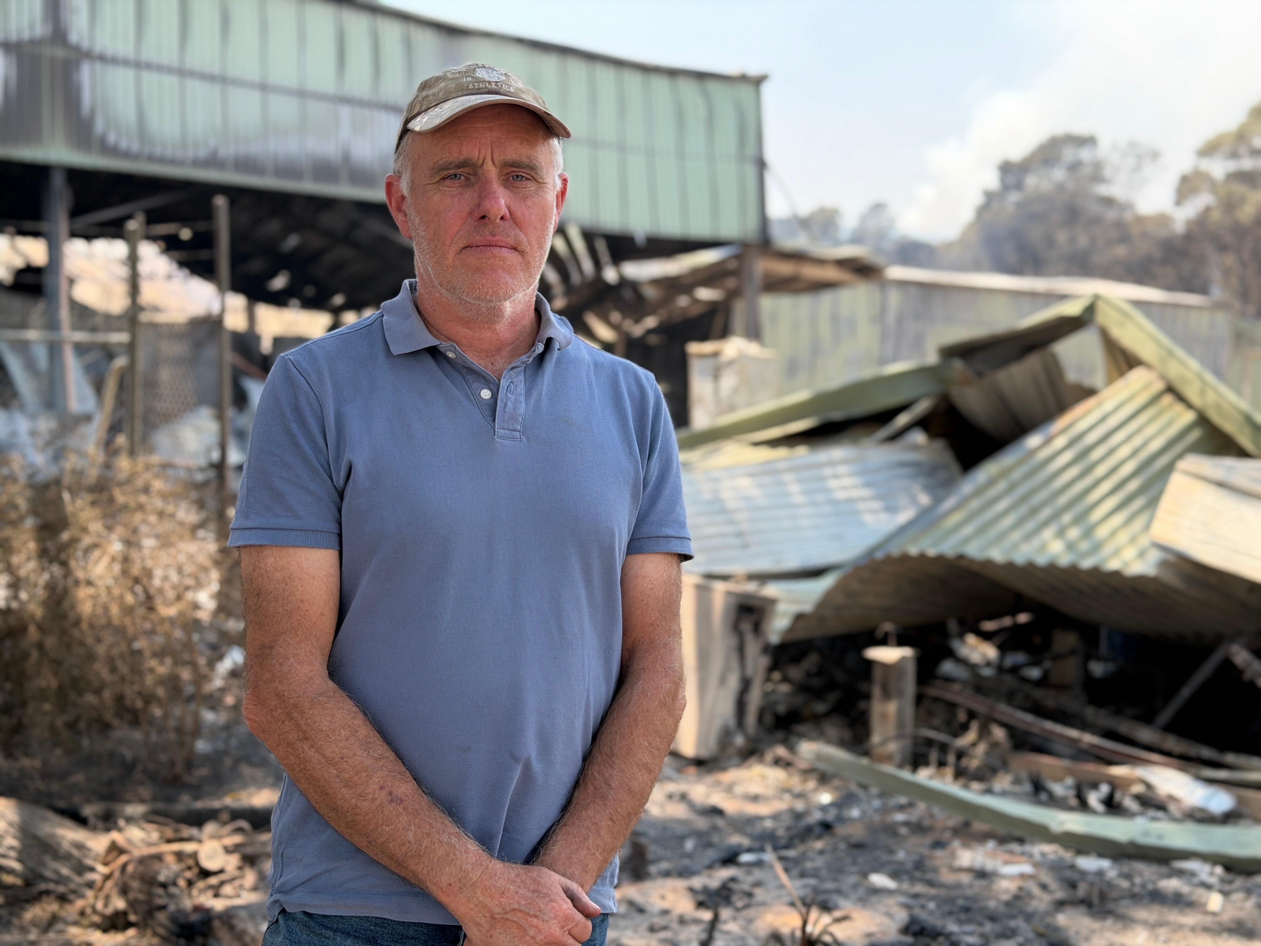 John Monteath se encuentra frente a un edificio quemado con una camisa azul.