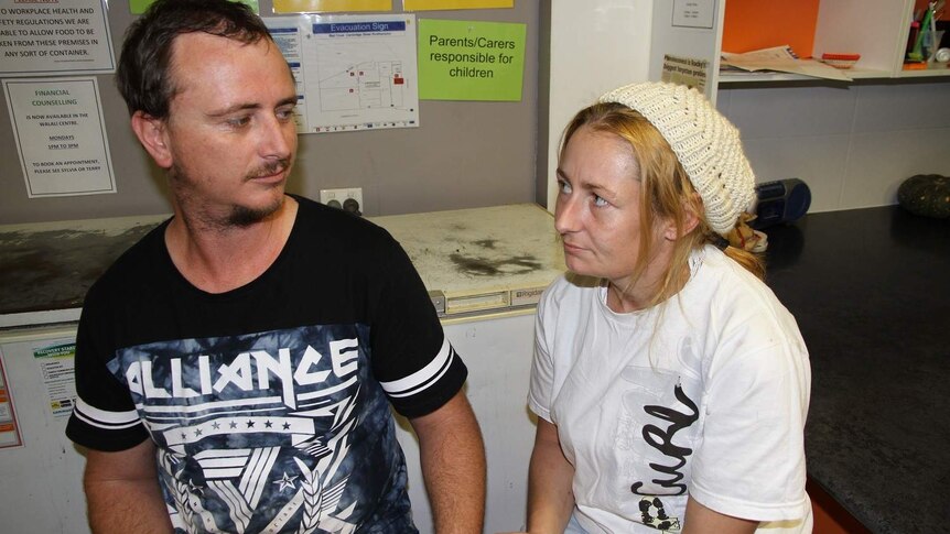 A man and woman look sadly into each other's eyes at a community centre.