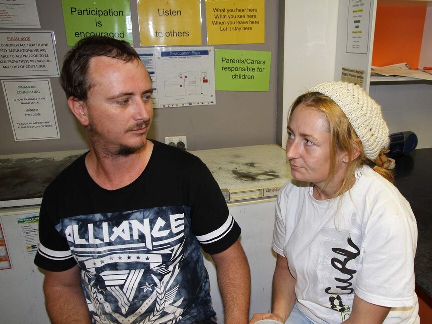 A man and woman look sadly into each other's eyes at a community centre.