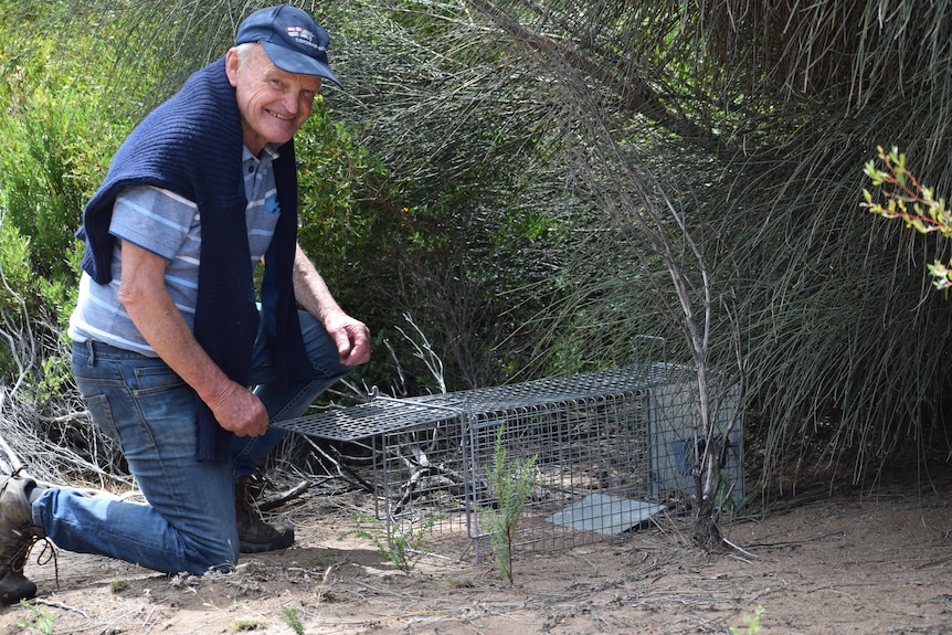 A man smiling at camera, kneeling on ground next to cat trap