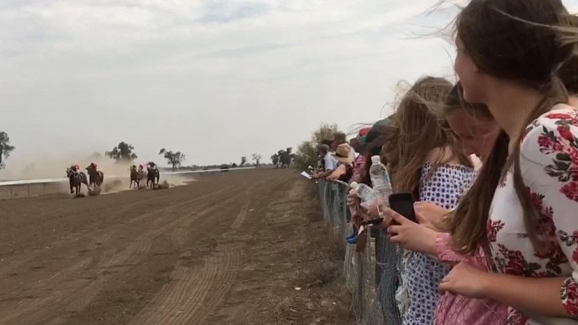 Horse kick up dust as they race past a crowd on the fence line