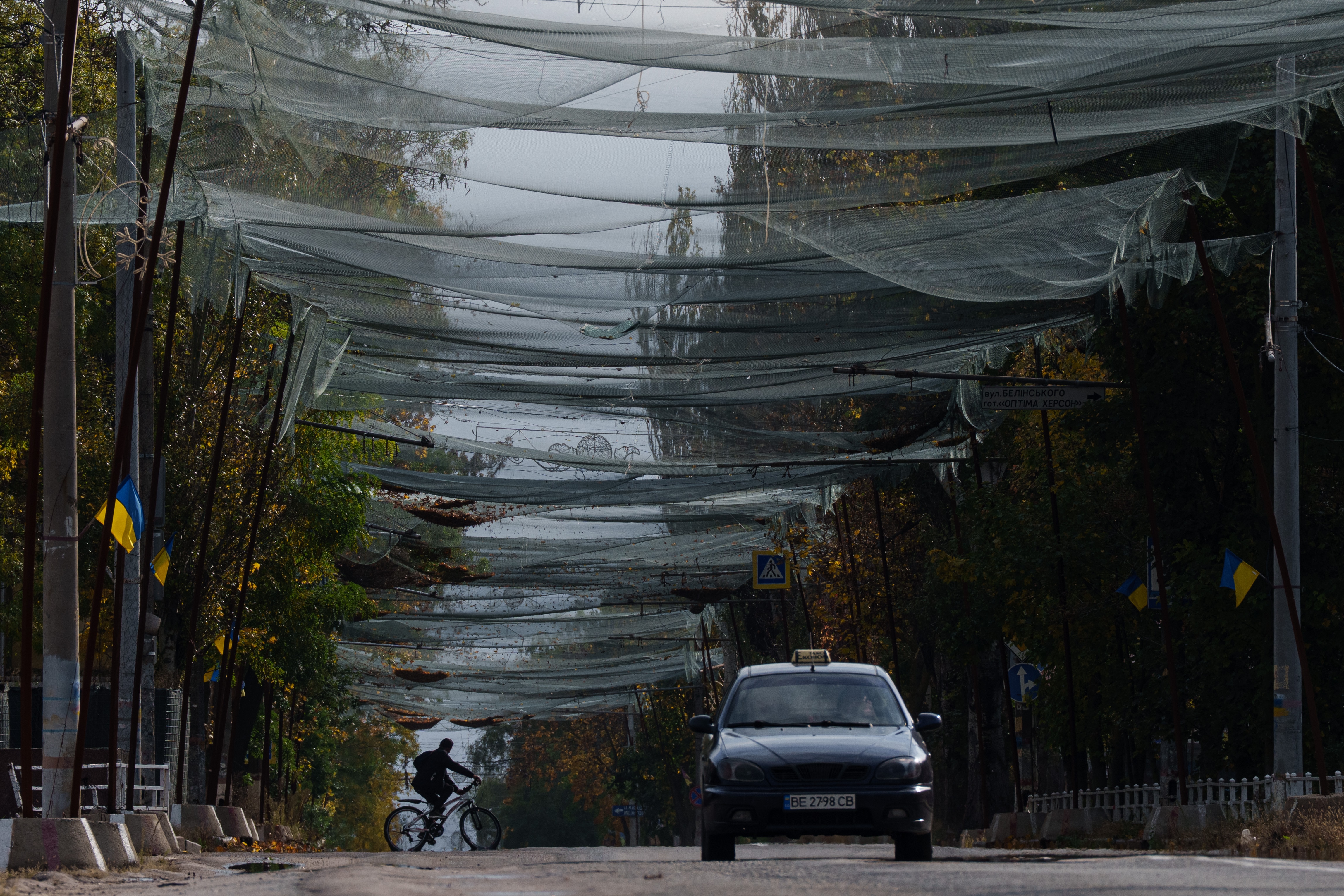 A man rides a bicycle on a deserted street draped with nets