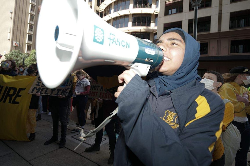 A person stands with protesters gathered behind them as they speak into a megaphone.