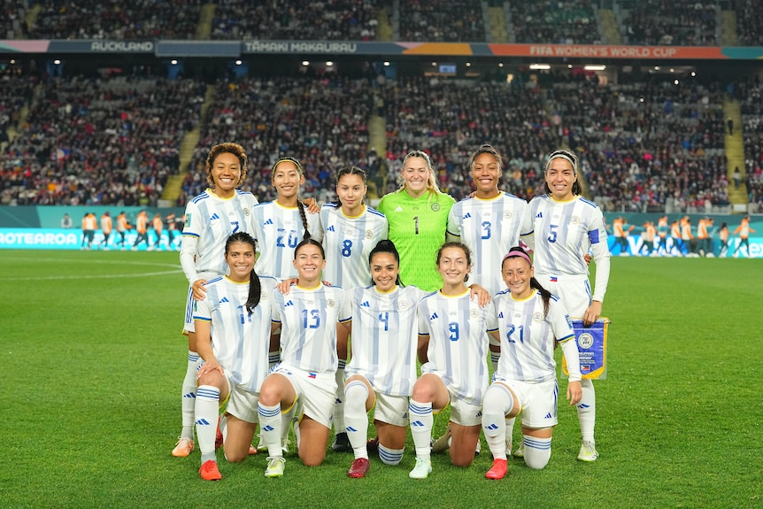 The Philippines women's national football team is lined up in two rows for a team photo on the pitch.
