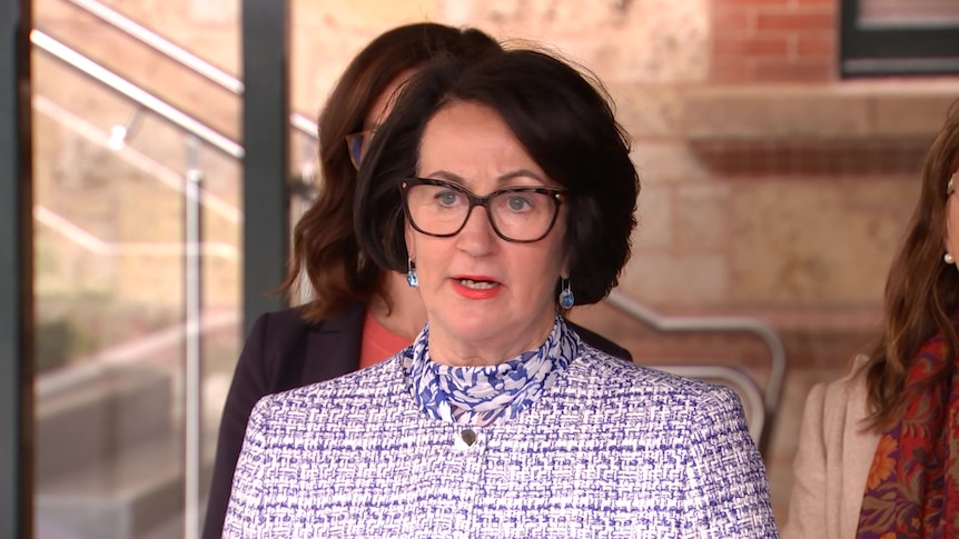 A woman with black glasses and black hair with another woman standing behind her