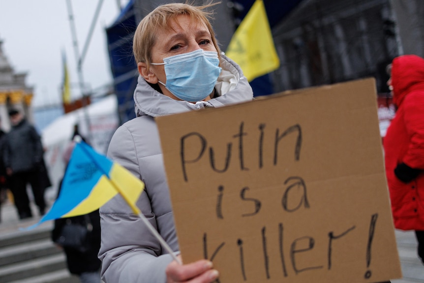 A woman holds a Ukrainian flag and a placard reading 'Putin is a killer'