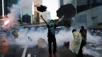 A protester raises his umbrellas in front of tear gas