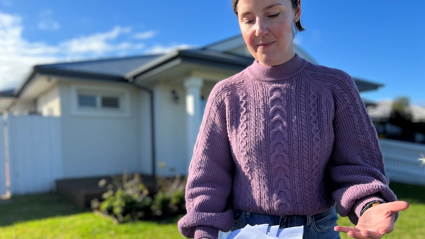 A woman holding bills outside a house 