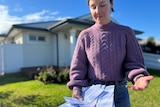 A woman holding bills outside a house 