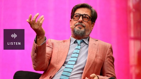 Roman Coppola gesticulates onstage, with a large LED wall behind him displaying a bright pink hue. . Has Audio.