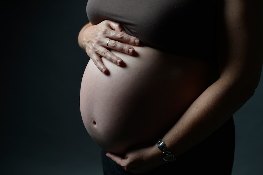 A woman's pregnant belly against a black background. 