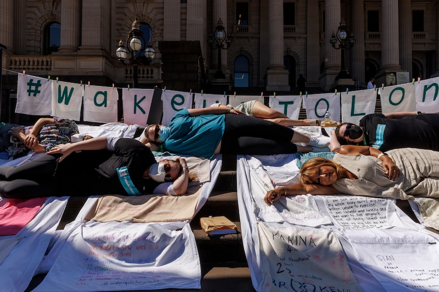 Several people laying on the steps of Parliament on top of pillowcases with the stories of sufferers from the illness. 