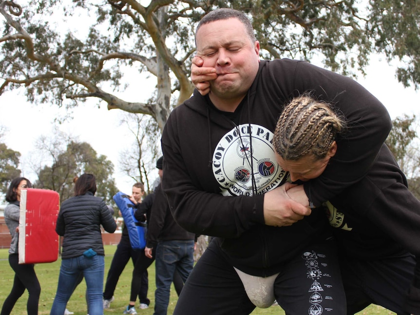 woman in headlock pulls at man's mouth with her finger