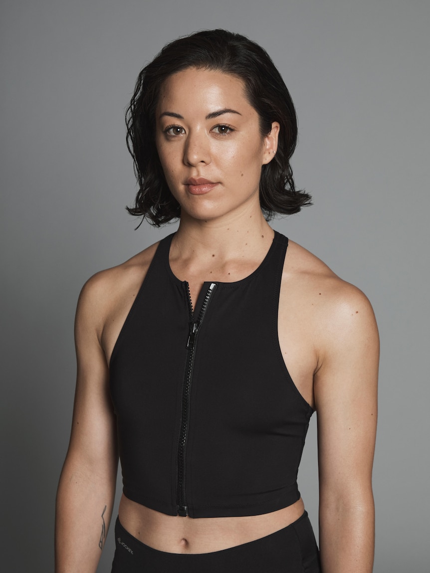 An athletic woman with dark hair wearing a black singlet poses for a photo with a serious expression on her face.