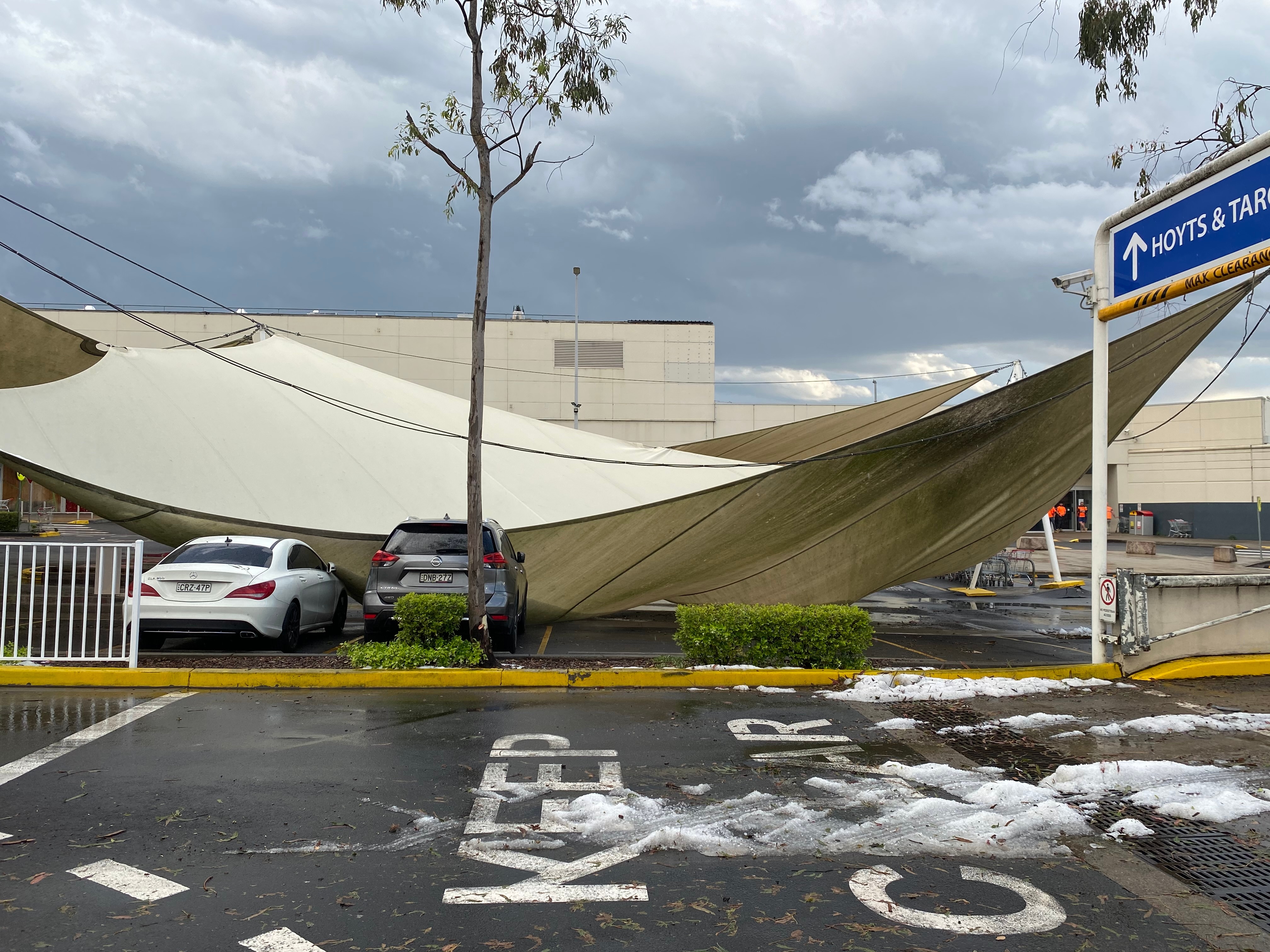 A large sunshade awning sags over two cars in a car park. 