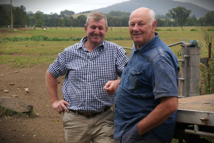 Two men standing on farm in front of gate between paddocks