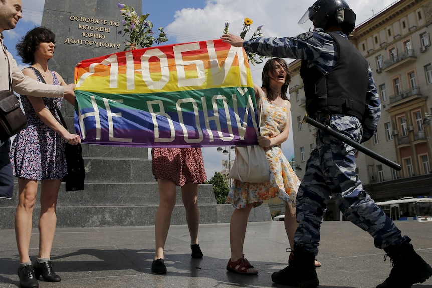 Four people hold a rainbow flag in central Moscow that says "Love. Don't make war". 