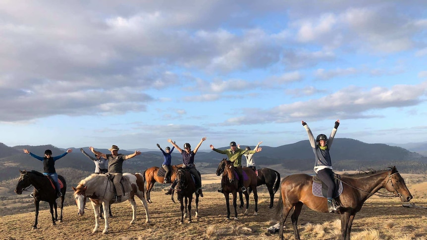 Eight people on horseback all with arms up in joy