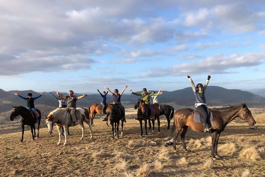 Eight people on horseback all with arms up in joy.