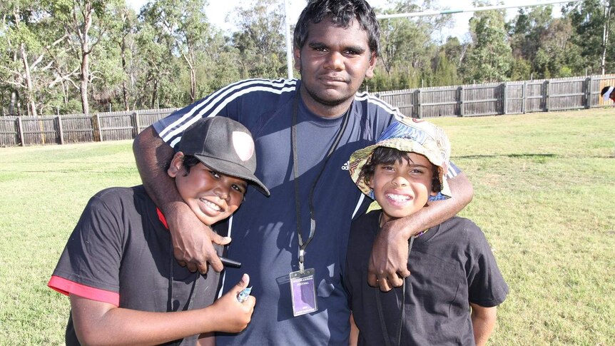 A teenager stands with his arms around two younger boys on a paddock.