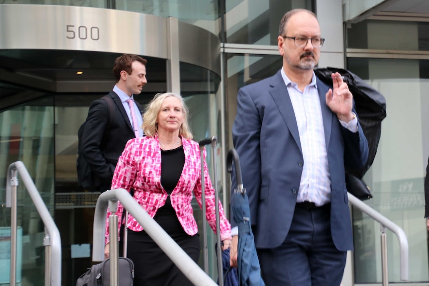 A besuited man walks ahead of a woman in a pink jacket and other men.