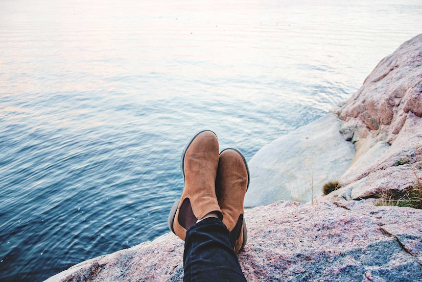 Person sitting on rock overlooking the calm ocean representing the need for rest and relaxation on a mental health day.