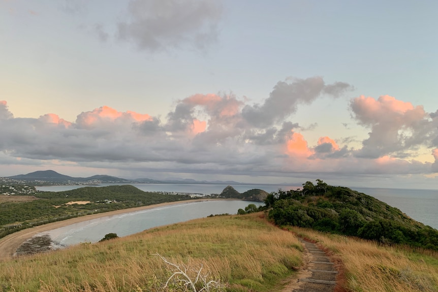 A path leading down a grassy mountain, ocean and other mountains in background.