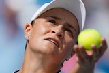Ash Barty throws a yellow tennis ball in the air with her left hand and looks up