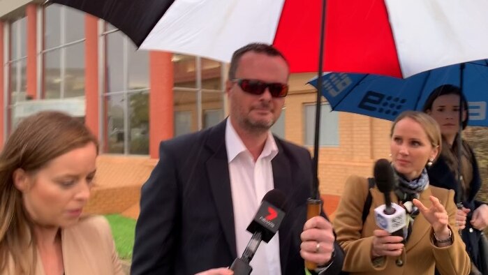 A man carrying an umbrella surrounded by reporters