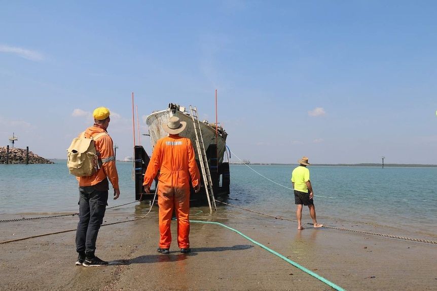Volunteers inspect the MV Rushcutter after floating it onto its trailer.
