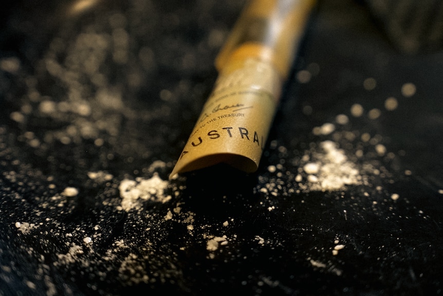 A rolled-up fifty dollar note sits surrounded by leftover cocaine residue on a black surface.