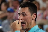 A tennis player holds his nose between points during a tennis match.