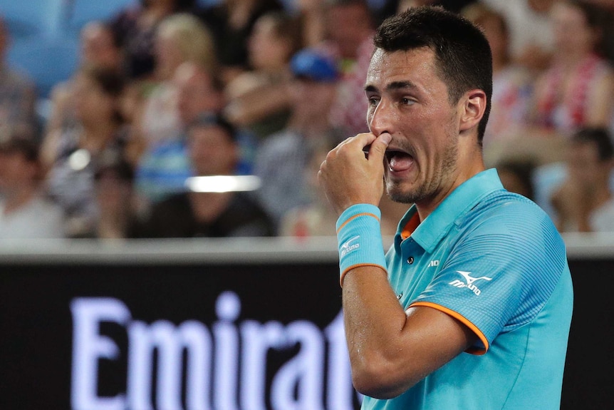 A tennis player holds his nose between points during a tennis match.