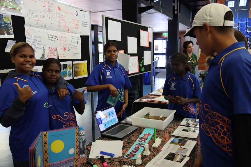 Five kids in blue school uniforms stand around a science display