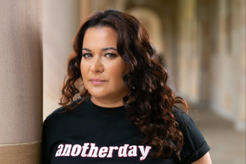 An Indigenous woman wearing a T-shirt with the words "another day in the colony" on it.