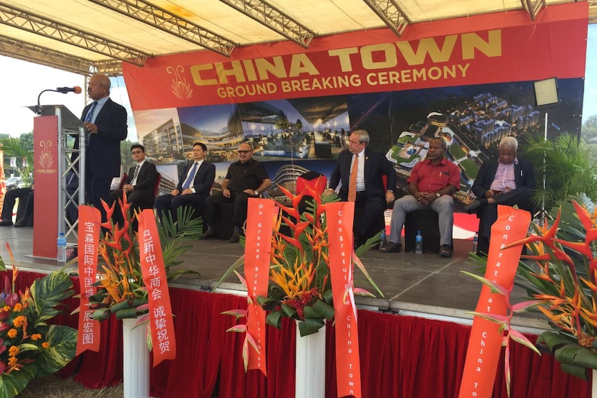 A man speaks on a stage in front of a banner that reads "China Town Ground Breaking Ceremony"