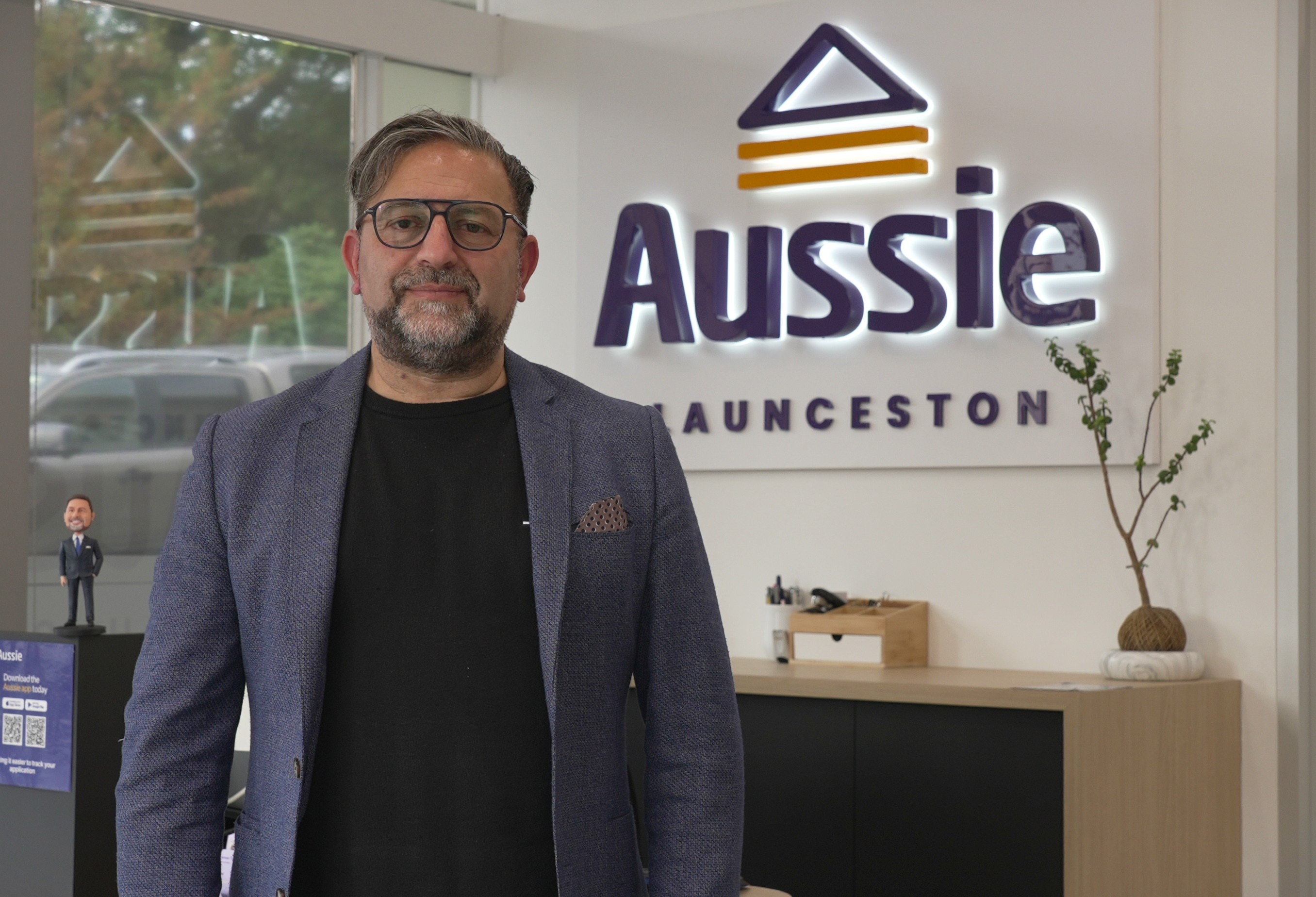 Chris Antypas stands in front of a purple and white sign that reads 'Aussie Launceston'.